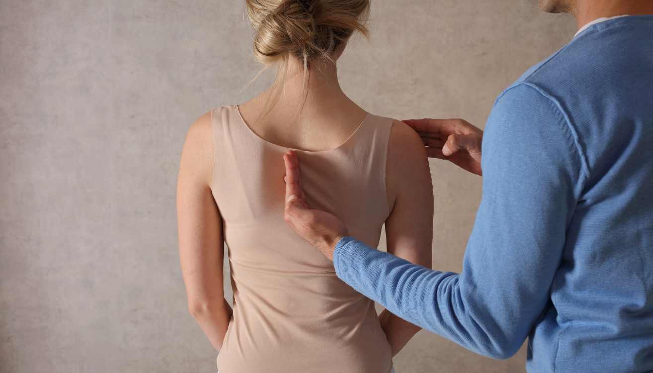 Therapeut zeigt auf Rücken einer Frau zur Analyse der Körperhaltung